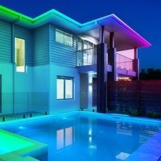 an illuminated pool in front of a modern house at night with lights on the windows