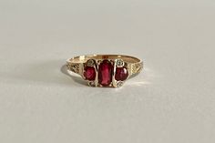 This is a gorgeous Edwardian Era 14k Yellow Gold Garnet Ring with a three genuine garnets and four white sapphire gemstone setting, the middle garnet is oval faceted cut the two side ones are faceted round cut, with four rose cut white sapphires one on each corner. A stunning piece of fine early 1900s era jewelry, featuring January's birthstone! ERA - Circa 1900s / Edwardian METAL / MATERIAL - 14k yellow gold, 3 genuine garnets (approx. 0.77 CTW), 4 white sapphires (approx. 0.02 CTW) MARKINGS / Vintage 14k Gold Ruby Ring With Accent Stones, Three Stone Ruby Ring In 14k Yellow Gold, Vintage Three-stone Ruby Ring Gift, Antique Three Stone 14k Gold Jewelry, Vintage Three Stone Ruby Ring Gift, Classic 14k Gold Three-stone Ruby Ring, Heirloom Ruby Ring With Three Stones In Round Cut, Vintage Three Stone Ruby Promise Ring, Vintage Three Stone 14k Gold Birthstone Ring