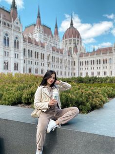 a woman is sitting on a ledge in front of a large building and drinking from a water bottle