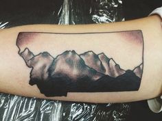 a man's arm with a black and white tattoo on it that has mountains in the background