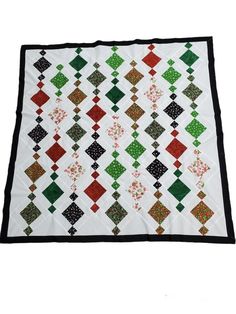 a white quilt with red, green and black squares on the bottom is laying down