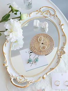 a white and gold tray with jewelry on it next to a flower bouquet, perfume bottle and ring box