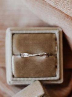 an engagement ring sitting in a box on top of a bed next to a pillow