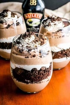 three glasses filled with dessert sitting on top of a wooden table next to a bottle