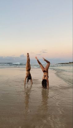 two women doing handstands on the beach at sunset with their feet in the water