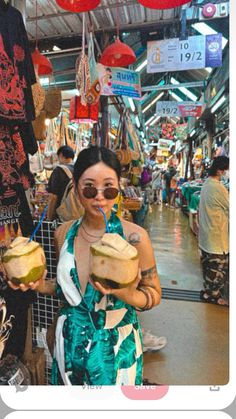 a woman holding two drinks in her hands while standing next to an open air market