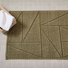 a bathroom rug on the floor next to a basket with towels and a white towel