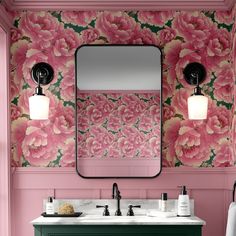 a bathroom with pink flowers on the wall and green cabinetry, along with a large mirror