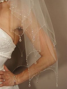 a woman wearing a wedding veil with beading on the bottom and side, holding her hands behind her back