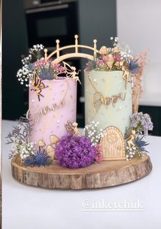 two cakes decorated with flowers and butterflies on a wooden stand in front of a kitchen