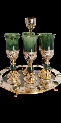 three green glass goblets sitting on top of a gold plate with two candles