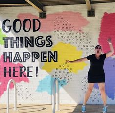 a woman standing in front of a wall with words painted on it that says good things happen here