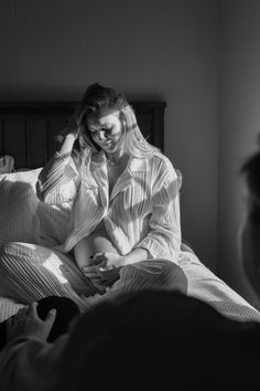 black and white photograph of woman sitting on bed with man looking at her in the background