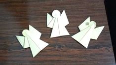 four pieces of paper cut out to look like angels on a wooden table with scissors