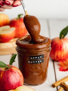 an apple butter in a jar being spooned into it with cinnamon sticks next to apples