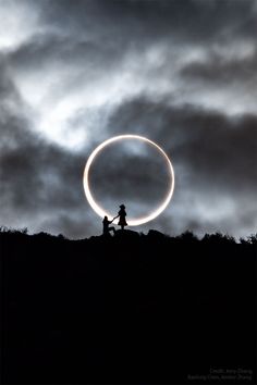 two people are sitting on a hill with a large circular object in the sky