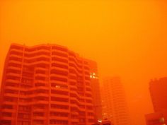 an orange colored sky with buildings in the foreground and cars on the street below