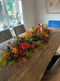 a wooden table topped with lots of flowers and greenery next to a blue chair