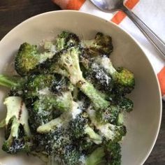 a white bowl filled with broccoli covered in parmesan cheese on top of a wooden table