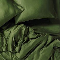 an unmade bed with green sheets and pillowcases on top of each other