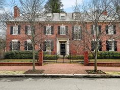 a large red brick house with black shutters on the front and side doors, surrounded by trees