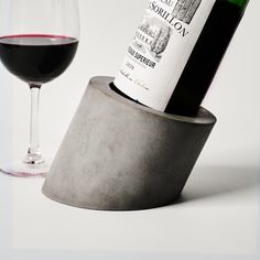 a bottle of wine sitting on top of a cement holder next to a glass of red wine