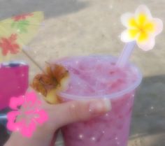 a hand holding a pink drink with an umbrella and flower on the top in front of it