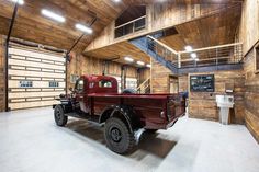 an old red truck is parked in a large garage with wooden walls and flooring