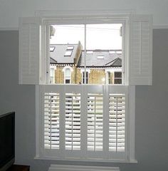 an empty living room with white shutters on the windows and a flat screen tv