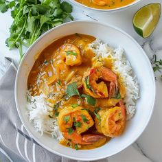 two bowls filled with shrimp and rice on top of a white tablecloth next to lime wedges