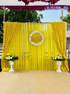 an outdoor ceremony with yellow drapes and white flowers on the stage, surrounded by greenery