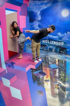 a man and woman standing in front of a hollywood mural