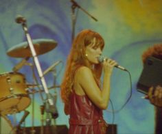 a woman singing into a microphone while standing next to a man with a guitar on stage