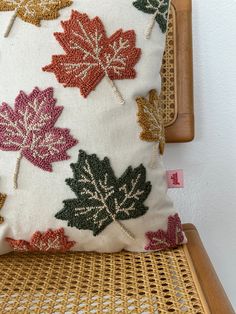 a decorative pillow on a wicker chair in front of a white wall and wooden frame