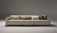 a couch with many pillows on it in front of a gray wall and grey floor