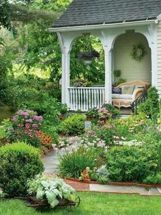 an outdoor gazebo surrounded by flowers and greenery in front of a white house