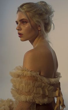 a woman with blonde hair wearing an off the shoulder ruffled dress and looking at the camera