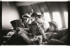 black and white photograph of people sitting in an airplane reading books while looking at something