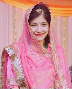 a woman wearing a pink and gold bridal outfit, smiling at the camera with her hands on her hips