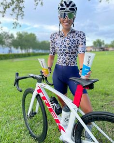 a woman is posing with her bike in the grass and holding an ice cream bar