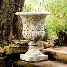 a large white vase sitting on top of a stone step next to a tree and rocks