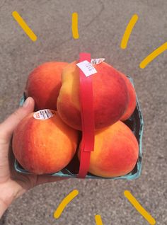 a hand holding a box filled with ripe peaches