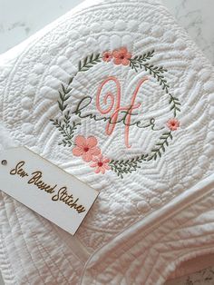 a white quilt with pink flowers and the letter qf on it is next to a price tag