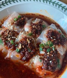 a white plate topped with dumplings covered in sauce and toppings on top of it