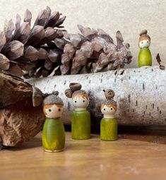 three little wooden dolls sitting next to a pine cone