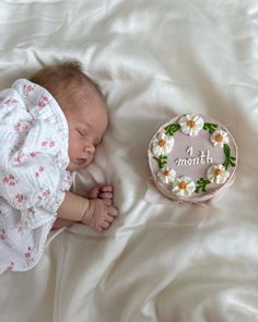 a baby sleeping next to a cake with flowers on it that says 4 month old