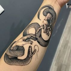 a hand with a snake tattoo on it's arm and the hands are holding an object