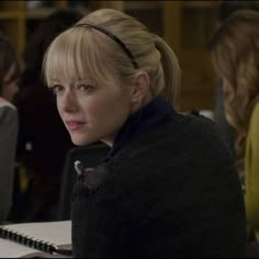 a woman sitting at a table with a notebook in front of her and other people behind her