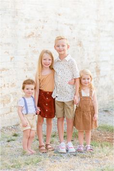 three young children standing next to each other in front of a wall and grass area