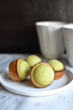 some green cupcakes on a white plate with two cups in the back ground